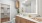 Bathroom area with wood cabinets, a large backlit mirror, and a white countertop, featuring a view into a walk-in closet with wooden shelves and hanging space